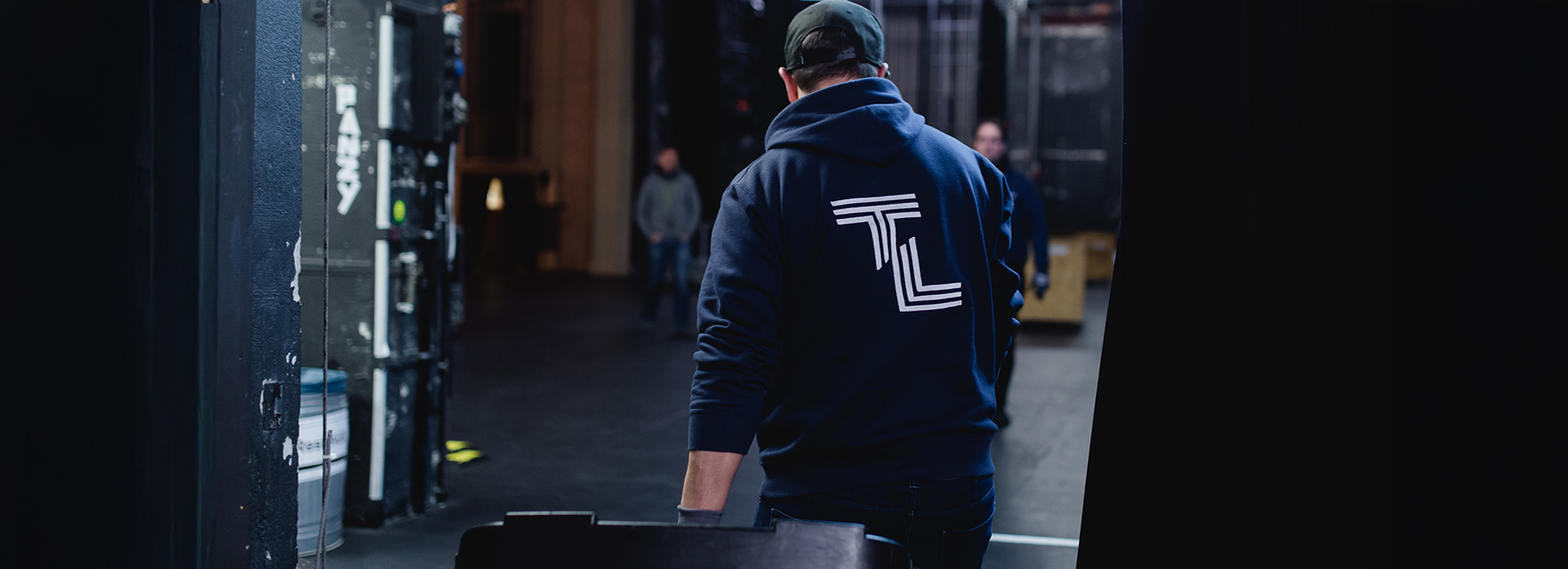 Auf Tour mit Theater Liberi Blick hinter die Bühne: Ein Techniker mit TL-Hoodie schiebt einen Transportkoffer durch den Bühnenbereich während des Aufbaus.