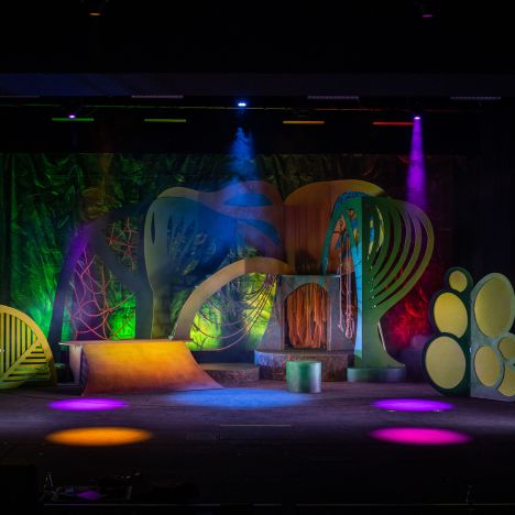 theater-liberi-tarzan-buehnenbild.jpg Beleuchtete, bunte Kulisse im Dschungelstil mit stilisierten Pflanzenformen.