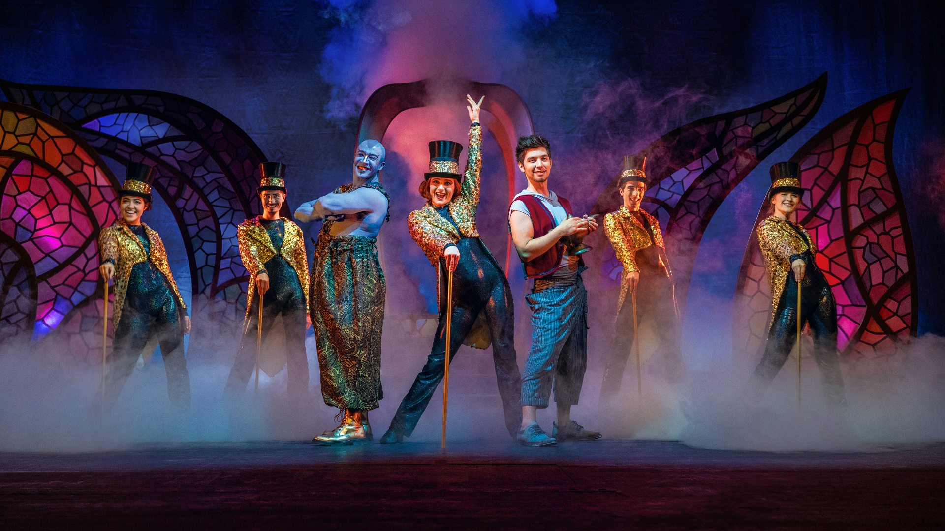 theater-liberi-aladin-ensemble-buehne-musical.jpg Ensemble von Theater Liberi in fantasievollen Kostümen auf der Bühne: Aladin, Dschinni und Tänzer:innen in Glitzeroutfits mit Zylindern, umgeben von Bühnennebel und orientalischem Bühnenbild.