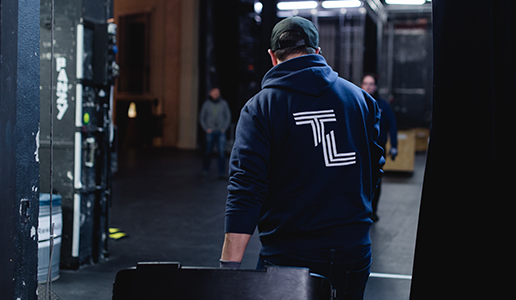 Auf Tour mit Theater Liberi Blick hinter die Bühne: Ein Techniker mit TL-Hoodie schiebt einen Transportkoffer durch den Bühnenbereich während des Aufbaus.