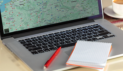 Planung im Büro bei Theater Liberi Laptop mit geöffneter Landkarte, daneben ein roter Stift, ein kariertes Notizbuch und ein Kaffee – Symbol für die Arbeit im Büro bei Theater Liberi.