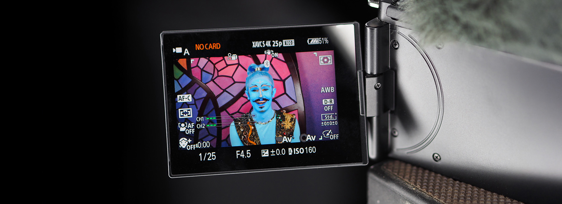 Interview mit einem Dschinni Kameradisplay zeigt fantasievoll geschminkte Bühnenfigur mit blauem Gesicht und orientalischem Kostüm vor buntem Mosaikhintergrund während einer Videoaufnahme.