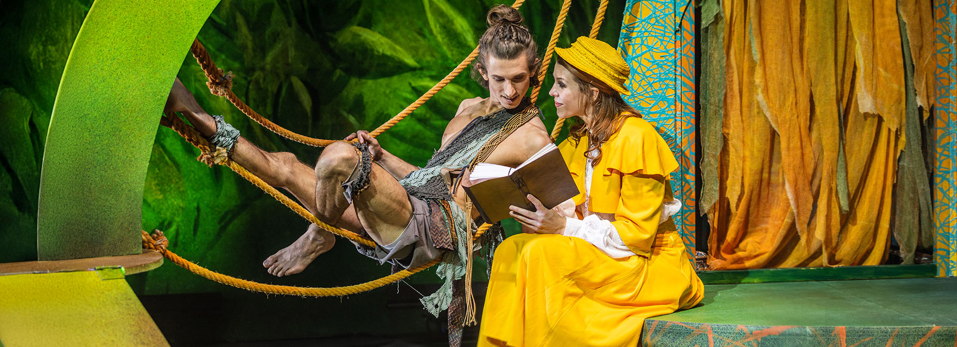 Tarzan und Jane in einer Szene aus „Tarzan – das Musical“ von Theater Liberi Tarzan liegt in Lianen, während er gemeinsam mit Jane ein Buch liest – Szene aus „Tarzan – das Musical“ von Theater Liberi