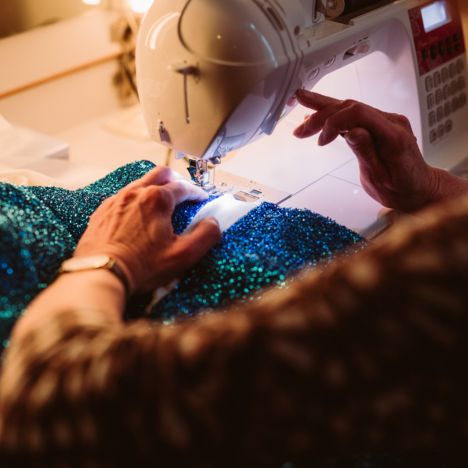 theater-liberi-kostuembild-naehmaschine-carolin-pommert Nahaufnahme einer Nähmaschine, an der eine glitzernde Bühnenrobe genäht wird.